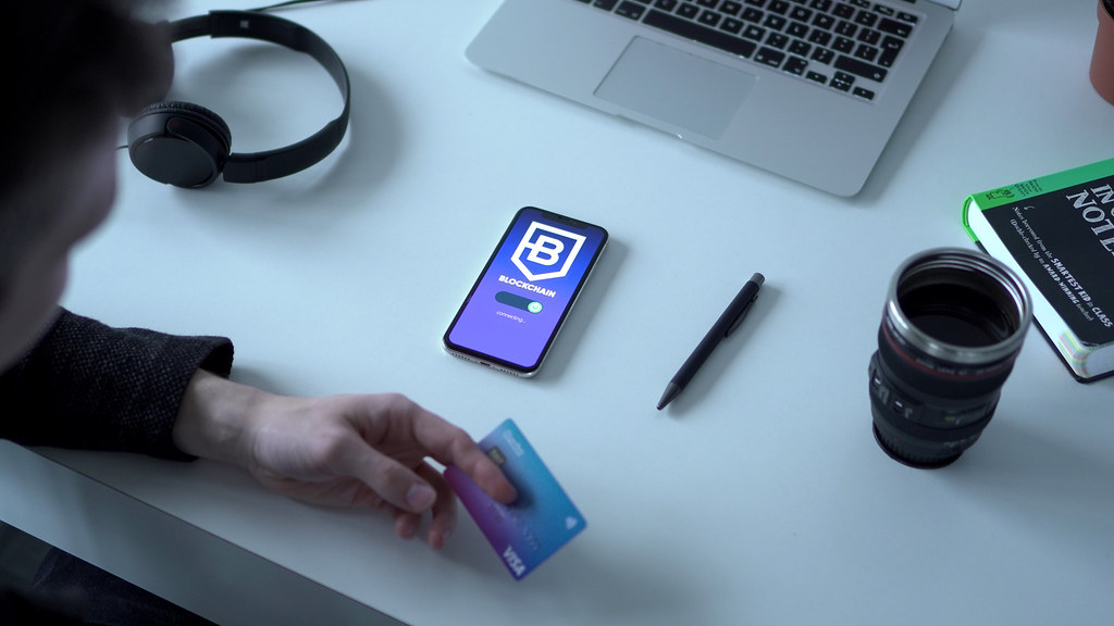 Desk with a laptop, phone, headphones, and a hand holding a payment card